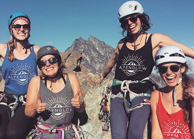Emily and her friends wearing their custom Alpenglow Collective tees atop a mountain.