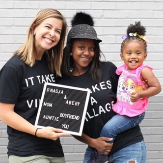 Dnasja smiling with a child in her arms whilst wearing t-shirts from the It takes a village campaign.
