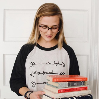 Holly Martin looking towards a pile of books that she is holding, whilst wearing her custom 3/4 sleeve baseball tee.
